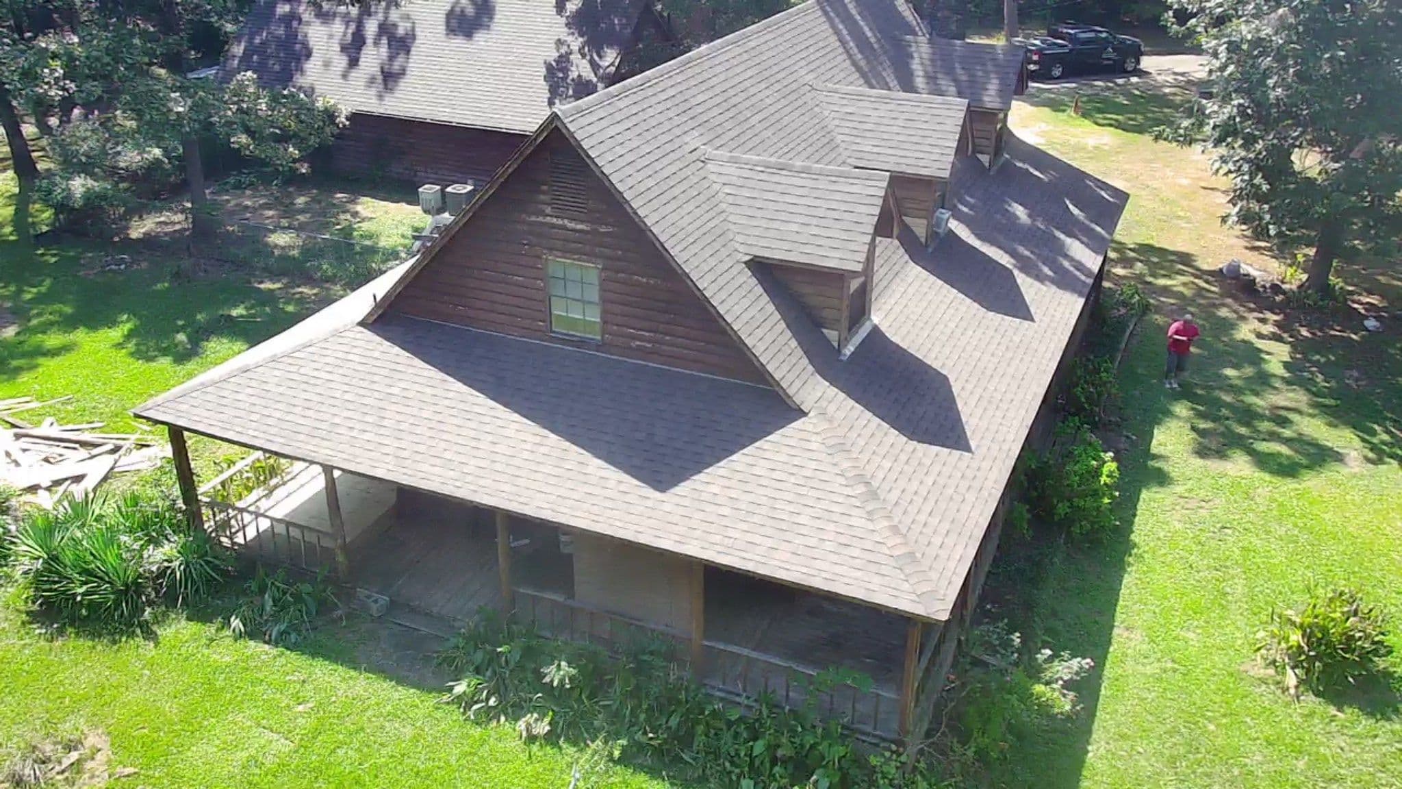 Aerial view of a rustic wooden house with a sloped roof and green surrounding landscape.